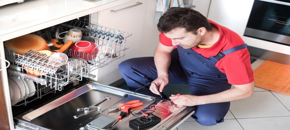 Professional worker repairing the dishwasher in the kitchen